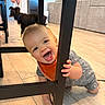 Braxton is registered to the contest to win money with this photo: baby, child, smiling, crawling, indoor, chair, floor, dog, pet, living_room, wooden_floor, furniture, happy, person, playful, orange_bib, gray_clothing, foot, background, home
