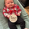baby, infant, plaid_shirt, black_pants, wooden_sign, three_months, smile, face, hand, feet, chair, green_fabric, flooring, home_interior, wooden_furniture, cute, child, portrait, sitting, indoors