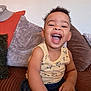 Caelen a rejoint le concours — aidez-le/la à gagner de superbes lots ! toddler, child, smiling, laughing, curly_hair, sitting, couch, pillows, indoor, yellow_tank_top, shorts, happy, playful, cute, home, living_room, arm, hand, person, young_child