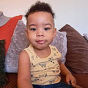 Caelen participe au concours pour gagner de l'argent avec cette photo : toddler, child, curly_hair, yellow_tank_top, denim_shorts, couch, pillows, indoor, casual_clothing, portrait, sitting, cute, young_child, relaxed, home, person, small_child, smiling, curious, comfortable