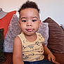 toddler, child, curly_hair, yellow_tank_top, denim_shorts, couch, pillows, indoor, casual_clothing, portrait, sitting, cute, young_child, relaxed, home, person, small_child, smiling, curious, comfortable