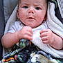 baby, infant, blanket, car_seat, child, face, hands, curious, indoors, portrait, safety_label, clothing, soft_texture, expression, young_child, seated, closeup, human, person, cute