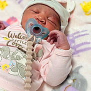 Naomi is registered to the contest to win money with this photo: baby, newborn, pacifier, sleeping, hat, pink_clothing, blanket, soft, cute, infant, child, resting, hand, face, indoors, cozy, pastel_colors, wearing_hat, cute_outfit, peaceful