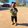 toddler, child, outdoor, sunny, smiling, green_sweatshirt, black_pants, tan_boots, standing, shadow, trees, car, hairstyle, playful, happy, daylight, casual_clothing, park, person, photography