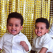 Yoas Et Noah a rejoint le concours — aidez-le/la à gagner de superbes lots ! toddler, child, smiling, white_shirt, sneakers, sitting, floor, gold_backdrop, happy, portrait, cute, indoor, two_children, curly_hair, casual_clothing, playful, young, people, friends, joy