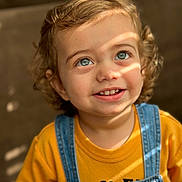 Bryan is registered to the contest to win money with this photo: toddler, child, smile, curly_hair, blue_eyes, yellow_shirt, denim_overalls, portrait, sunlight, indoor, happy, cute, young_child, face, person, clothing, casual, expression, closeup, baby