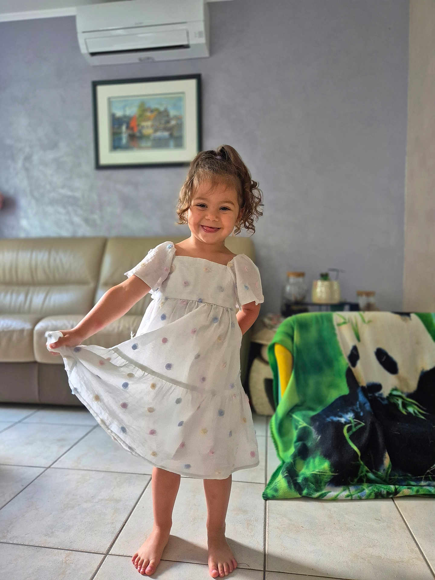 Hel participe au concours pour gagner de l'argent avec cette photo : child, girl, dress, smile, barefoot, living_room, sofa, blanket, panda, tile_floor, curly_hair, painting, air_conditioner, furniture, home_interior, playful, happy, person, portrait, casual