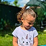 child, girl, smiling, curly_hair, ponytail, tshirt, unicorn, cat_face, outdoor, garden, sunny, greenery, blue_sky, casual_clothing, sitting, happy, cute, daylight, playful, nature