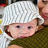 adult, affection, baby, close_up, cuddle, eyes, face, family, green_sweater, holding, indoor, infant, mother, photography, portrait, safe, smiling, soft_lighting, striped_clothing, sunhat