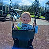 child, toddler, swing, playground, smiling, happy, outdoor, daylight, park, clothing, holding, green, sippy_cup, sky, trees, slide, play_equipment, fun, joy, person