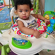 Koa is registered to the contest to win money with this photo: toddler, child, baby, activity_center, toy, curly_hair, indoor, colorful, play_area, carpet, person, cute, looking, sitting, clothing, footwear, floor, plastic, baby_toy, expression