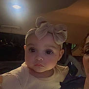 Marisol joined the competition — help win amazing prizes! baby, child, headband, bow, face, eyes, clothing, sitting, indoor, car, seat, person, portrait, cute, infant, expression, soft_lighting, young, apparel, closeup
