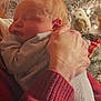 newborn, baby, sleeping, person, hand, christmas_tree, ornament, holiday, cozy, warm_clothing, indoor, soft_lighting, celebration, red_sweater, decorations, festive, peaceful, portrait, close_up, family_moment