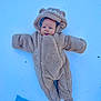 baby, child, snow, winter, onesie, costume, fuzzy, cute, outdoor, cold, face, tongue, blue, warm_clothing, lying_down, playful, headwear, person, infant, animal_ears