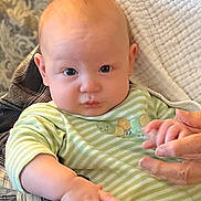 Jace is registered to the contest to win money with this photo: baby, infant, child, face, eyes, cheeks, onesie, green_stripes, hand, adult_hand, holding_hands, blanket, quilt, portrait, closeup, indoor, cute, expression, looking_at_camera, soft_lighting