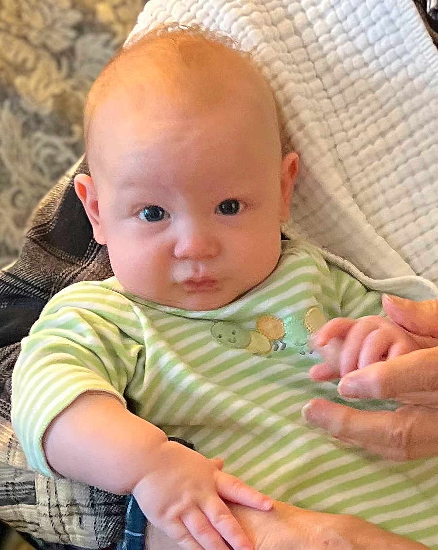 Jace is registered to the contest to win money with this photo: baby, infant, child, face, eyes, cheeks, onesie, green_stripes, hand, adult_hand, holding_hands, blanket, quilt, portrait, closeup, indoor, cute, expression, looking_at_camera, soft_lighting