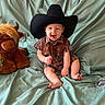 Jace is registered to the contest to win money with this photo: baby, belt_buckle, bull, child, cowboy_boots, cowboy_hat, cute, footwear, green_fabric, hat, indoors, infant, plaid_clothing, plant, portrait, sitting, smiling, soft_toys, stuffed_animal, western_theme