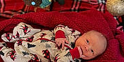 Jace joined the competition — help win amazing prizes! baby, newborn, infant, blanket, red, christmas_tree, pajamas, holiday, festive, carpet, decorations, ornament, plush, sleepwear, cute, indoors, child, face, lying_down, cozy