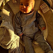 Tommy participe au concours pour gagner de l'argent avec cette photo : baby, infant, baby_seat, blanket, clothing, cozy, cushion, face, indoor, infant_clothing, light, person, portrait, relaxing, seat, shadow, soft_texture, socks, sunlight, warm_light