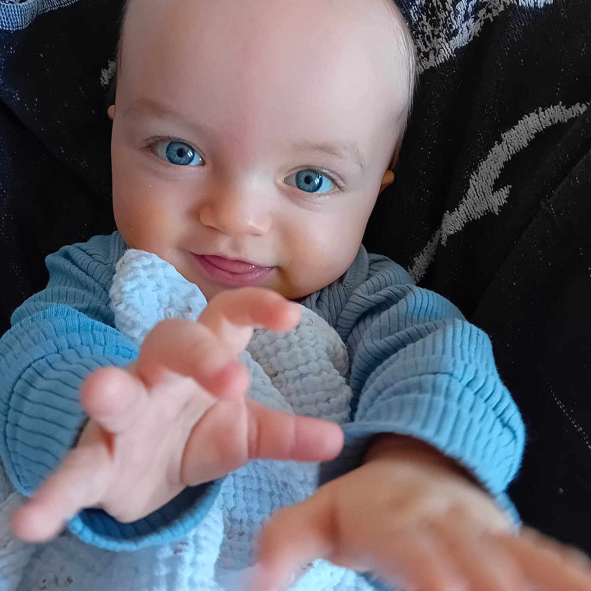 Tommy participe au concours pour gagner de l'argent avec cette photo : baby, child, blue_eyes, reaching_hand, smiling, blanket, blue_clothing, closeup, portrait, infant, cute, happy, indoor, soft_texture, face, person, young_child, cozy, expression, skin