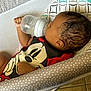 baby, bottle, mickey_mouse, onesie, infant, baby_seat, polka_dots, curly_hair, feeding, indoor, child, cute, relaxed, soft_light, toddler, cuddly, sleepy, comfort, smiling, closeup