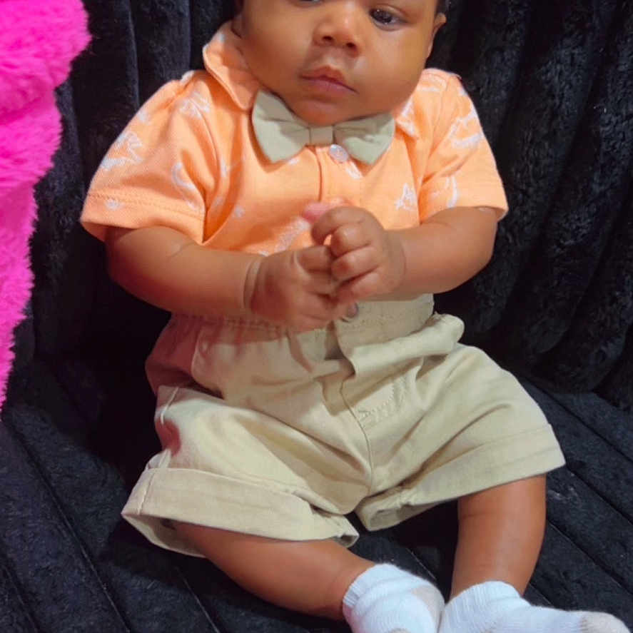 Rahzel is registered to the contest to win money with this photo: baby, infant, child, sitting, clothing, bow_tie, shorts, socks, black_background, pink_object, cute, portrait, indoors, young_child, fashion, hands_clasped, soft_texture, small_sock, serious_expression, photography