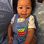baby, child, smile, curly_hair, toy_story, overalls, blue_clothing, sitting, blanket, personalized_blanket, name, happy, cute, indoor, portrait, young_child, hand, face, eyes, infant