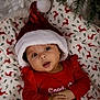 baby, child, santa_hat, christmas, holiday, festive, red_clothing, blanket, reindeer_pattern, ornament, tree, indoors, cute, infant, portrait, holiday_season, smiling, hands, face, cozy