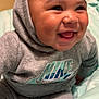 baby, infant, smiling, hoodie, nike, grey_clothing, happy, cute, closeup, indoors, soft_blanket, sitting, child, face, portrait, young, joyful, cozy, apparel, expression