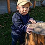 Timéo a rejoint le concours — aidez-le/la à gagner de superbes lots ! toddler, child, outdoor, grass, tree_stump, wood, hat, cap, clothing, navy_sweater, jeans, shoes, person, nature, daylight, fence, curious, baby, hands, standing