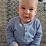 toddler, child, baby, blue_shirt, jeans, sitting, couch, patterned_fabric, indoor, portrait, smiling, cute, face, hands, short_hair, light, casual_clothing, young_child, home, curious