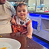 baby, child, adult, restaurant, table, plate, food, buffet, lighting, smile, face, hair, necklace, clothing, person, indoor, furniture, holding, cute, happy