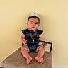 Brittany is registered to the contest to win money with this photo: baby, child, girl, sitting, chair, bow, necklace, black_top, denim_shorts, barefoot, indoors, yellow_wall, wooden_floor, cute, portrait, person, casual_clothing, infant, young_child, calm_expression