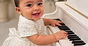 Brittany is registered to the contest to win money with this photo: baby, child, piano, white_dress, bow, smiling, indoor, flower_arrangement, music, playing, cute, portrait, happy, infant, celebration, soft_lighting, decor, elegant, toddler, closeup
