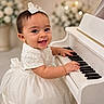 baby, child, piano, white_dress, bow, smiling, indoor, flower_arrangement, music, playing, cute, portrait, happy, infant, celebration, soft_lighting, decor, elegant, toddler, closeup