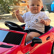 Julio participe au concours pour gagner de l'argent avec cette photo : baby, blurred_background, child, cute, face, garden, happy, necklace, outdoor, playing, portrait, red_car, seatbelt, short_sleeves, smiling, steering_wheel, sunlight, toy_car, wheel, white_tshirt