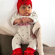 Nami a rejoint le concours — aidez-le/la à gagner de superbes lots ! baby, blanket, child, clothing, couch, cozy, cute, flower_headband, footwear, headwear, indoor, infant, person, polka_dot_pajamas, portrait, red_booties, red_headband, serious_expression, sitting, soft_toys
