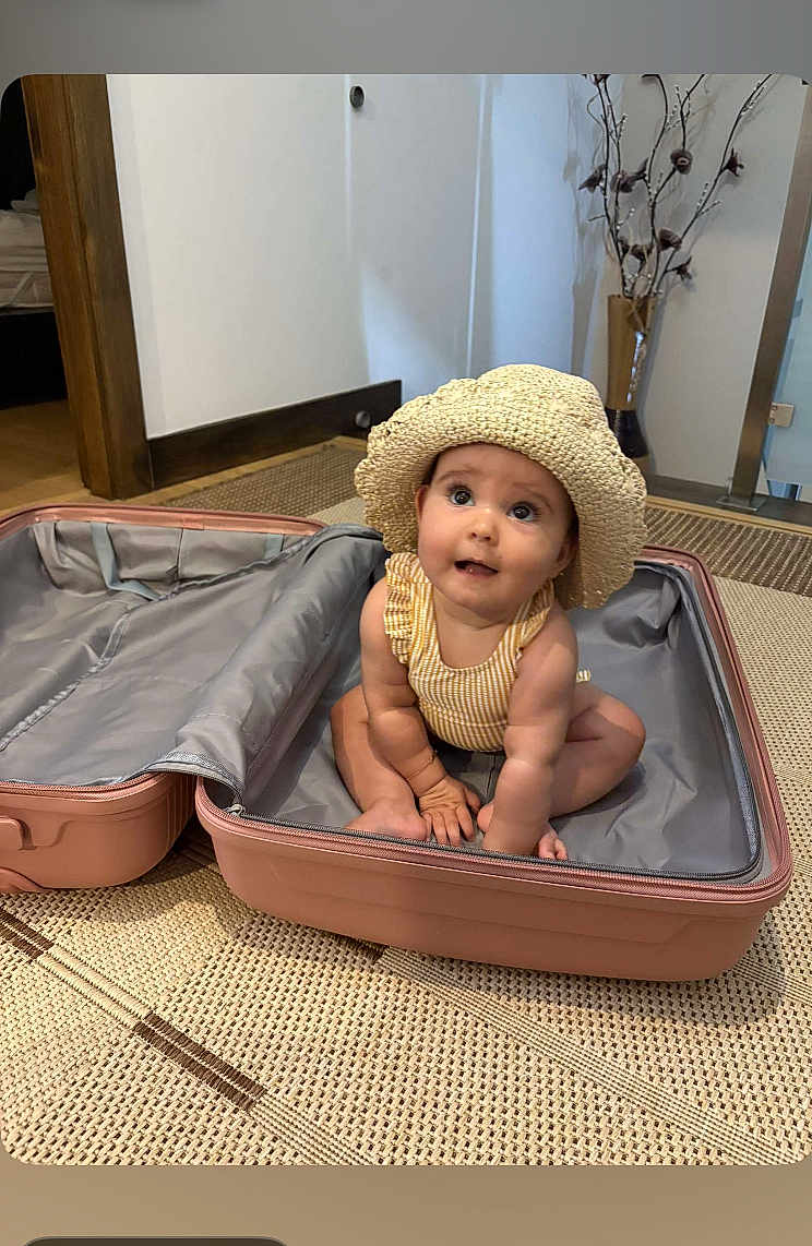 Elena participe au concours pour gagner de l'argent avec cette photo : baby, child, suitcase, hat, straw_hat, indoor, floor, rug, curious, seated, cute, looking_up, pink, travel, open_suitcase, woven_rug, home, innocent, small, adorable
