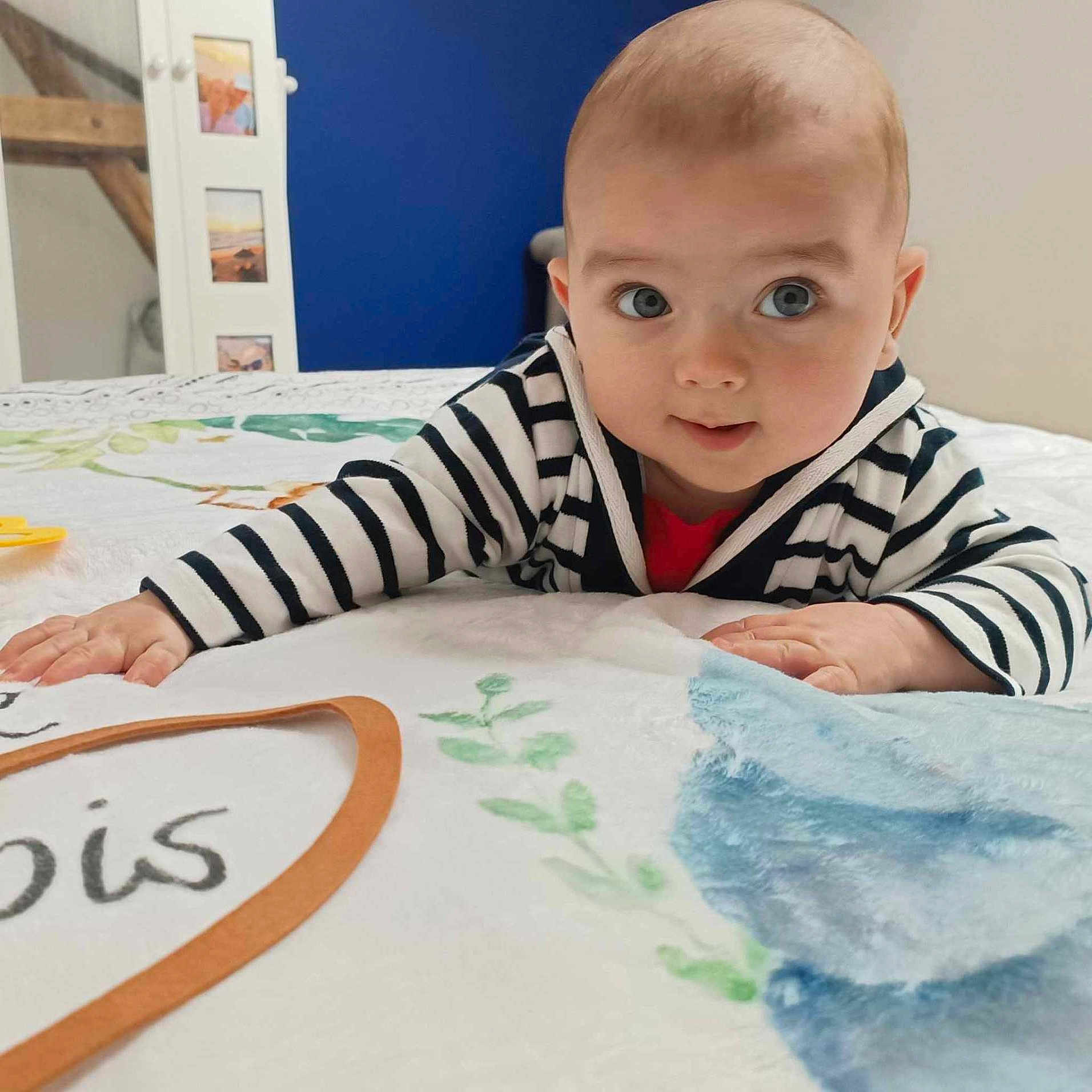 Soan participe au concours pour gagner de l'argent avec cette photo : baby, bed, blanket, blue_wall, child, crawling, curious, cute, expression, eyes, face, floral_pattern, furniture, hand, hoodie, indoor, person, photograph, room, striped_clothing