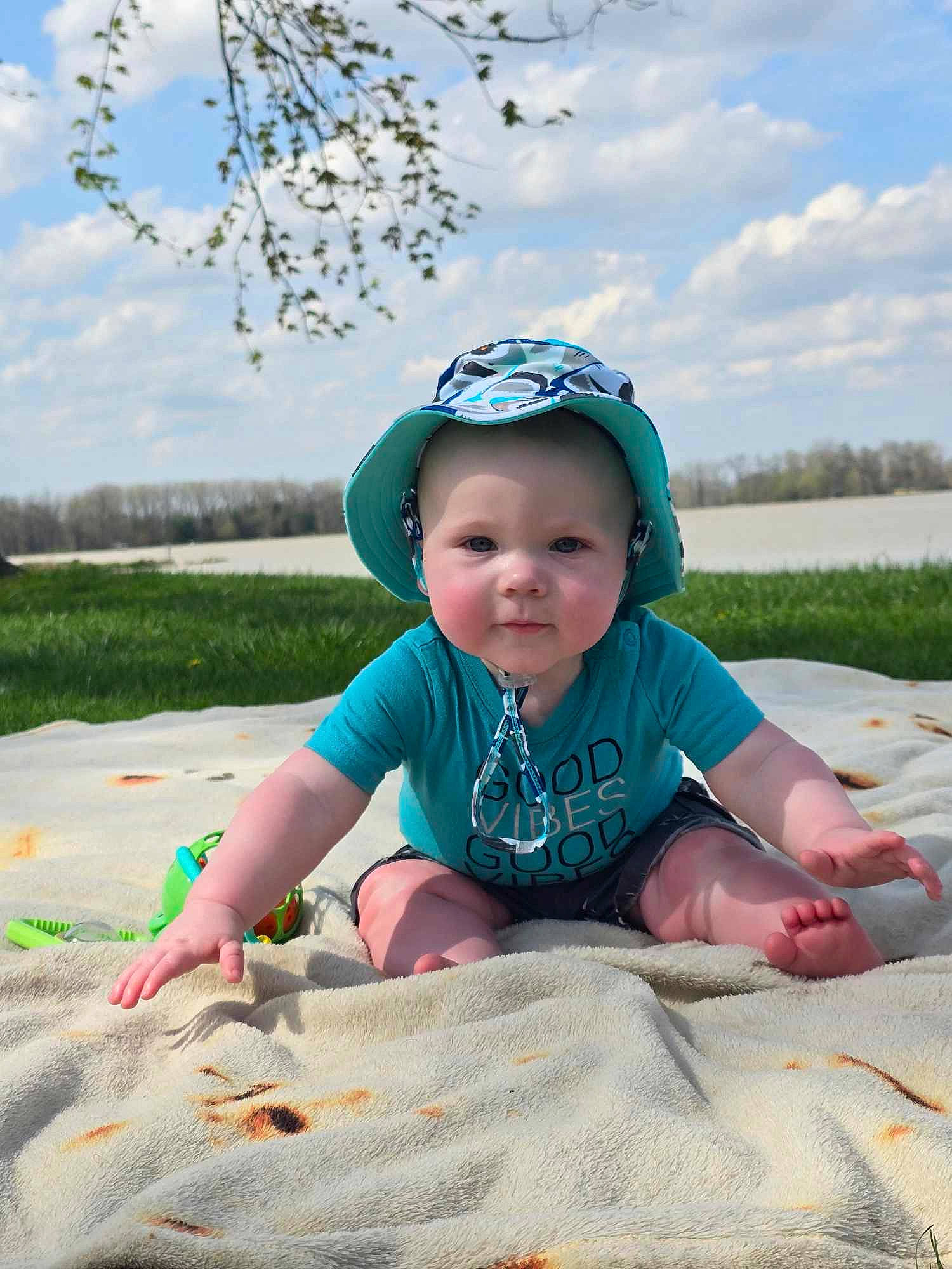 Kingston is registered to the contest to win money with this photo: baby, baby_toddler_clothing, cap, cloud, grass, happy, hat, headgear, headwear, landscape, leisure, people_in_nature, person, plant, recreation, sitting, sky, sleeve, smile, t_shirt