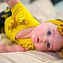 baby, child, face, blue_eyes, yellow_clothing, headband, portrait, skin, infant, cute, soft_light, close_up, lying_down, bed, fabric, expression, curious, person, indoor, newborn