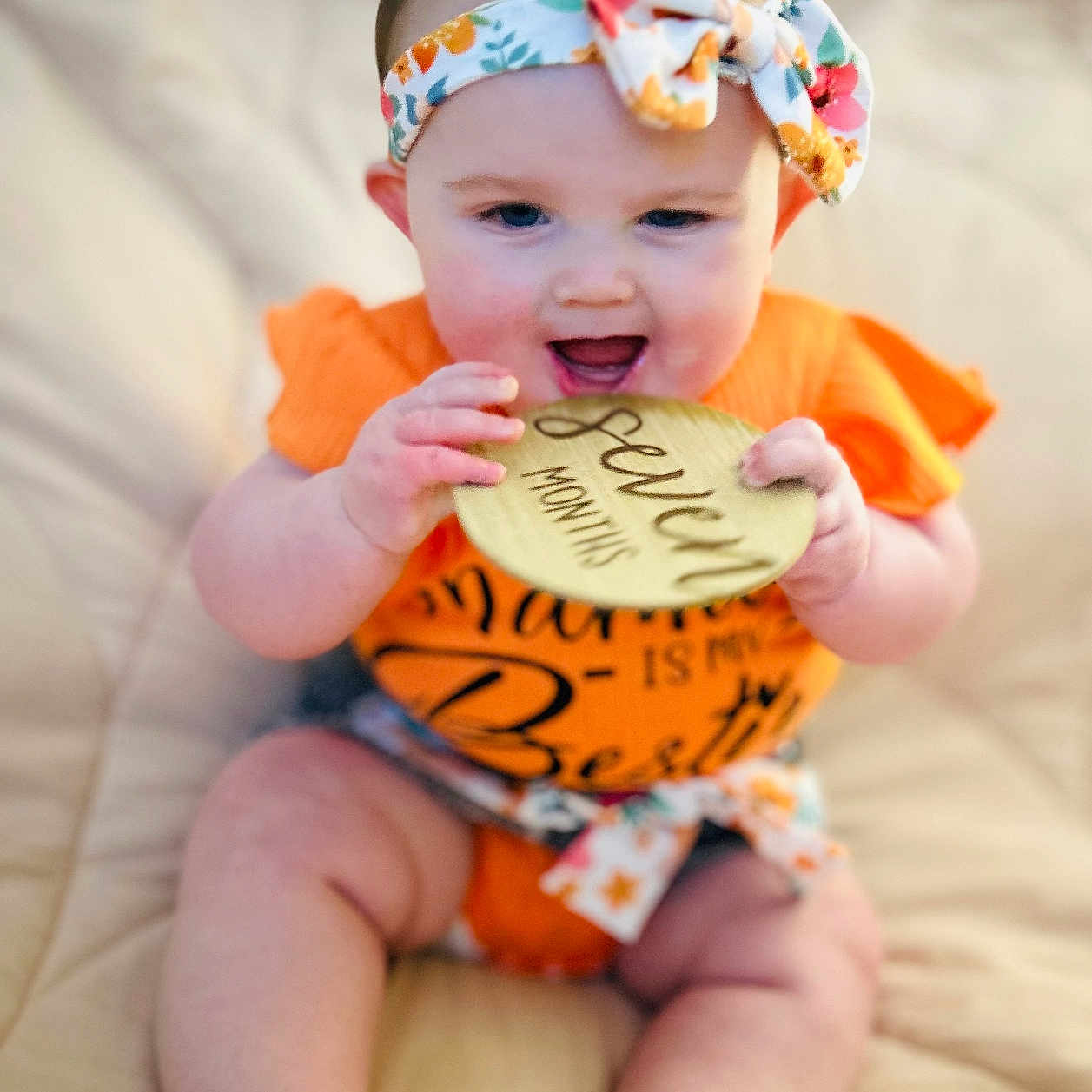 Ezlynn is registered to the contest to win money with this photo: baby, barefoot, child, cute, face, feet, floral_pattern, hand, headband, indoors, infant, milestone, orange_clothing, portrait, seven_months, sitting, skin, smiling, soft_blanket, wooden_plaque