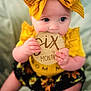 Ezlynn is registered to the contest to win money with this photo: baby, infant, child, six_months, yellow_bow, yellow_outfit, wooden_sign, milestone, chewing, cute, sitting, soft_blanket, indoor, portrait, closeup, happy, face, hands, feet, young