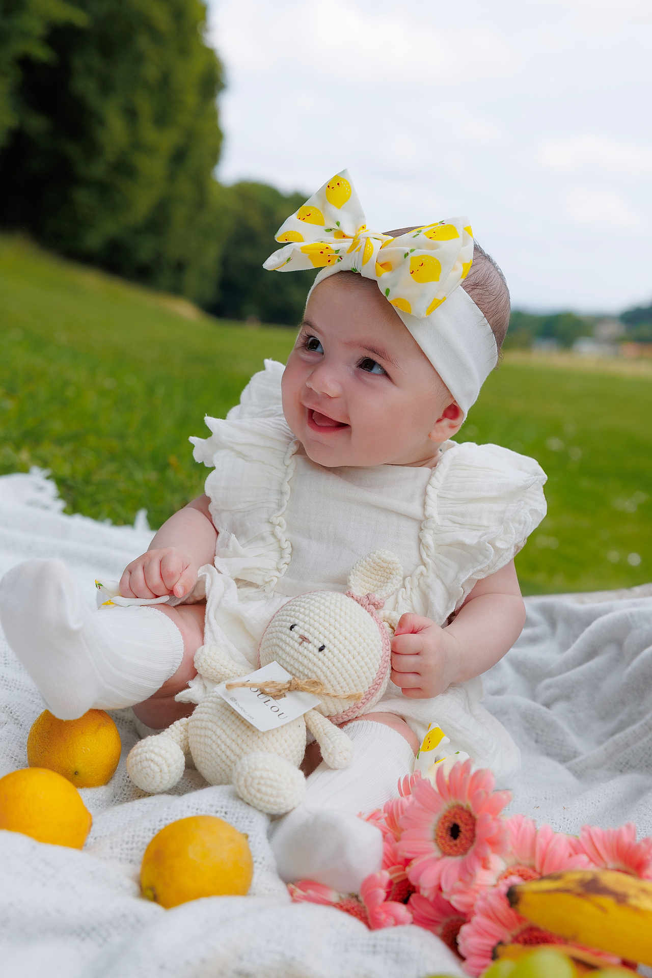 Sophie a rejoint le concours — aidez-le/la à gagner de superbes lots ! baby, child, outdoor, grass, blanket, headband, bow, toy, crocheted_toy, lemons, flowers, pink_flowers, white_clothing, socks, smiling, happy, nature, fruit, portrait, cute
