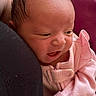 baby, newborn, infant, pink_clothing, person, face, head, expression, closeup, indoors, pillow, fabric, human, skin, curly_hair, soft_light, candid, holding, comfort, cute