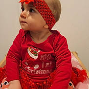 Lilou a rejoint le concours — aidez-le/la à gagner de superbes lots ! baby, child, red_clothing, headband, bow, christmas_theme, festive, sitting, cute, indoor, infant, portrait, holiday, cushion, pattern, looking_up, long_sleeve, toddler, decorative, young_child