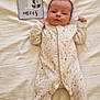 Matéo participe au concours pour gagner de l'argent avec cette photo : baby, infant, one_month, onesie, milestone_card, bed, white_sheet, lying_down, raised_fists, calm, curious, indoor, soft_lighting, floral_pattern, newborn, cute, child, portrait, sleepwear, human