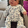 Matéo a rejoint le concours — aidez-le/la à gagner de superbes lots ! baby, infant, onesie, dog_pattern, sitting, person, indoor, couch, living_room, curious, wide_eyes, legs, hand, furniture, blanket, footed_pajamas, home, casual, soft_lighting, relaxed