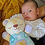 baby, infant, plush_toy, stuffed_animal, blanket, couch, white_clothing, soft_toy, indoor, child, person, cute, cozy, resting, face, head, expression, holding, comfort, home