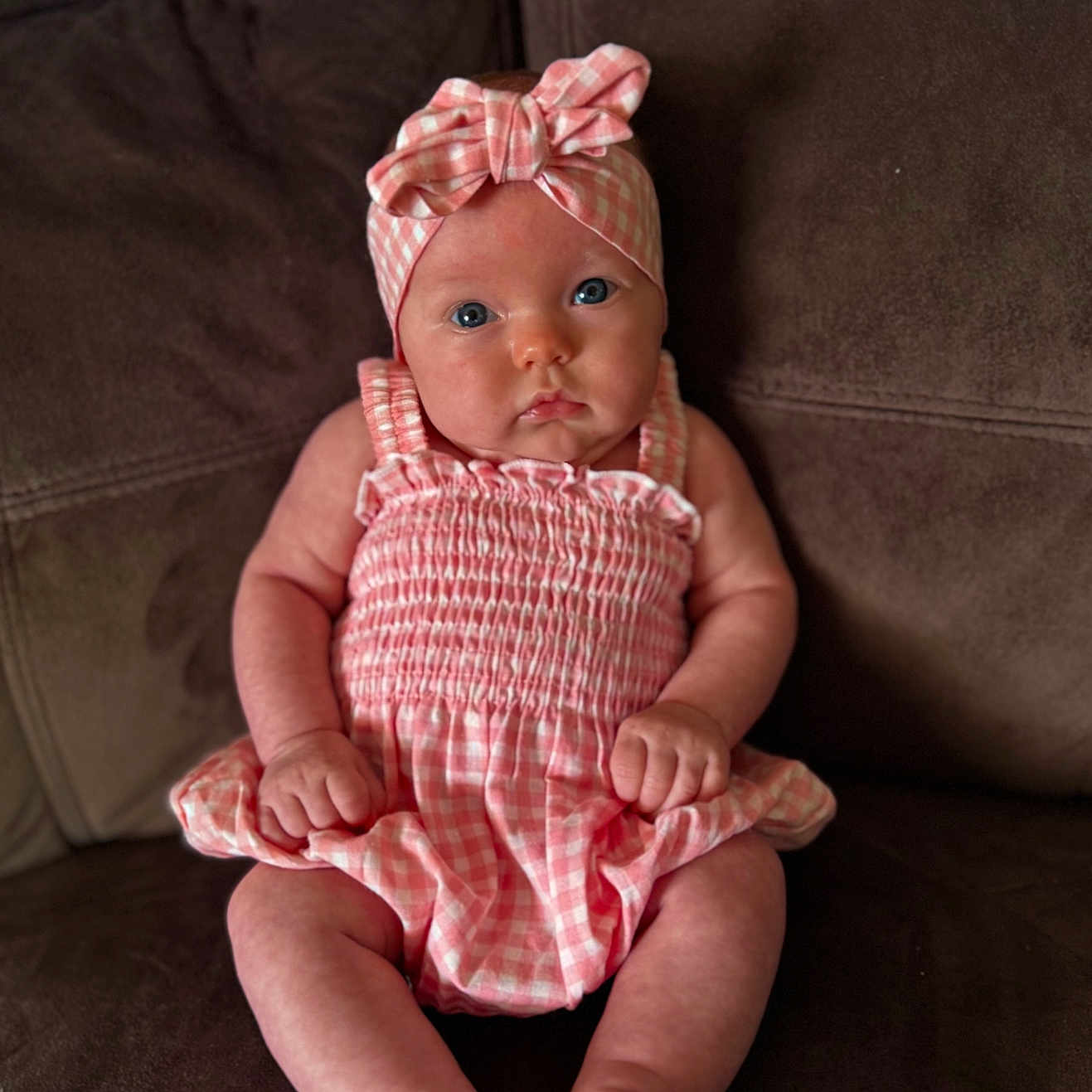 Adeline joined the competition — help win amazing prizes! baby, infant, child, pink_clothing, headband, blue_eyes, sitting, couch, brown_furniture, indoors, cute, portrait, chubby_cheeks, fist, gazing, soft_lighting, plaid_pattern, young, person, cozy